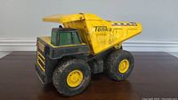 Side view of vintage Tonka dump truck toy showing yellow dump bed, black front grille, and green cab windows