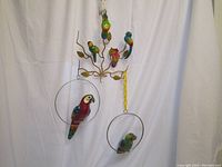 Wide view of wall mounted metal tree with 4 colorful parrots on branches and 2 large parrots in metal rings hanging on yellow chain.