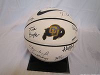 White Nike basketball with Colorado Buffalo logo and multiple signatures from coaches and players, displayed on a black stand