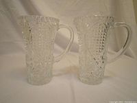 Front view of two clear crystal water pitchers showing textured geometric patterns and handles.