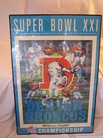 Overall front view of the framed Super Bowl XXI poster showing the Denver Broncos players, logo and text.