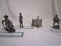 Wide-angle photo showing all three pewter figurines (Pecos Bill, Uncle Sam, Paul Bunyan) and the small pewter building, all displayed against a white background.