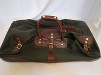 Full view of dark green canvas rolling bag with brown leather buckles and handle