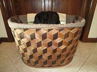 Lateral side view of large wicker basket, showing brown wood pattern with fabric lining at top edge.
