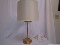 Full view of the table lamp showing clear glass body, brass base, and white shade with included power cord.