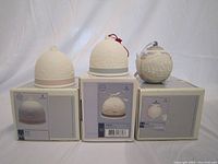 Three Lladro Christmas porcelain bells displayed on their original boxes against a plain backdrop. Box images show the bells' designs.