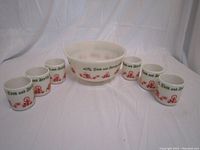 Photo showing six cups arranged around the large bowl, all decorated with festive Tom and Jerry text and holiday images in red and green on opaque white glass.