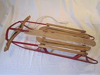 Full side angle view of vintage wooden Champion sled with red metal runners and steering bar.