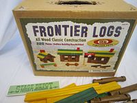 Original box of Ideal Frontier Logs wooden construction set showing branding, piece count (220 pieces), and sample models constructed from the logs.
