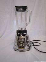 Full frontal view of the vintage Osterizer blender showing glass pitcher, lid, and power cord.