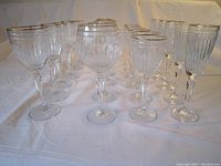 Front view of all 24 Waterford Marquis crystal wine glasses arranged on a white cloth showing four distinct sizes and vertical cut patterns with gold rims.
