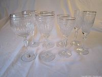 Eight Waterford Marquis crystal wine glasses shown upright on a white cloth with lighting. The glasses show a vertical ribbed pattern with gold rim accents, arranged in groups of two by size.