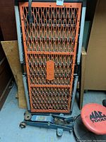 Full view of the VIKA portable platform folded and leaning with blue car jack and MAC stool