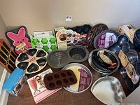 Wide view of multiple cake pans and molds including pink bunny pan, heart slice pans, round pans, silicone molds.