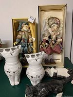Two fabric dressed cat dolls in original Katherine's Collection boxes with tags, two ceramic cat vases with heart cut-outs, and a black and white ceramic cat figurine lying down all displayed together.