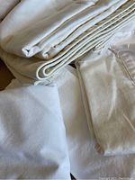 Close up of folded cream and white bed linens including sheets and mattress protector.