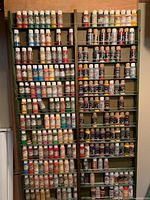 Two tall shelving units packed with rows of assorted acrylic paint bottles of various brands and colors