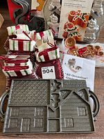 Full lot showing cast iron gingerbread house mold, ceramic gingerbread man measuring spoons, boxed gingerbread man pan, striped fabric towels, and printed instructions.