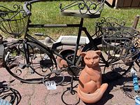 Photo showing a black metal bicycle plant holder and terracotta ceramic cat plant holder.
