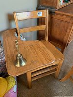 Wooden school desk with brass bell on seat, showing wood grain and brass bell details