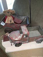 Red metal toy truck and wagon with vintage-style cloth bear seated inside the wagon. Showcasing general condition and color.
