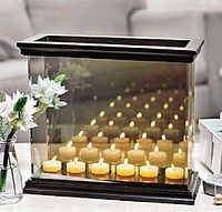 Decorative black wooden framed tea light candle holder with mirror back reflecting rows of lit candles to create an infinity effect.