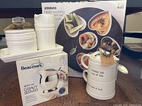 Full view of all items in lot including Stokes revolving condiment set packaging, Beaumark gravy server box, and Mud Pie cream, sugar, and tea cup set.