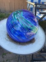 Photo of large decorative garden glass ball resting on a metal birdbath in outdoor setting.