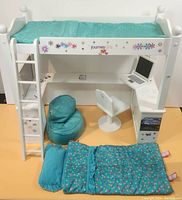 Front view of white wooden doll bunk bed with ladder and desk below. Includes turquoise bedding, bean bag chair, pillow, sleeping bag, white swivel chair, and laptop on desk.