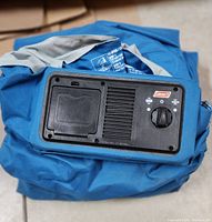 Blue Coleman air mattress folded and showing the attached inflation pump with control dial and battery compartment.