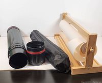 Photo of wooden paper roll holder with white paper roll, black storage bag, and hard plastic cylindrical case