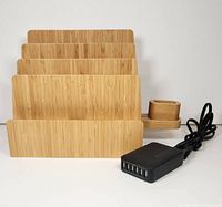 Front view of bamboo charging station showing four vertical slots and side earbud holder with black 6-port USB charger and cable