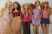 Five dolls standing, showing full body and outfits under natural light