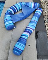 Big Joe pool floats photo showing striped blue and white noodle sling with a seat and armrests placed on poolside tiles.