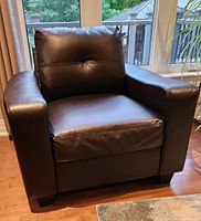 Front angled view of dark brown faux leather armchair showing cushioned backrest and wide arms with minor surface damage.