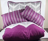 Close-up view of two purple and white patterned throw pillows with one grey and white chevron pillow sham behind them.