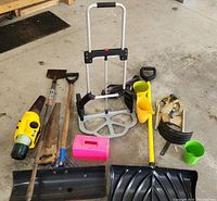 Overview of all garden tools and accessories including shovels, sprinkler, mosquito fogger, folding dolly, toolbox and others placed on a concrete floor.