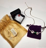 All three jewelry pieces displayed together: copper cuff bracelet in gold pouch, red and silver ring charm in black box, Avon charm necklace with purple pouch