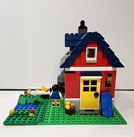 Front view of the assembled Small Cottage build with recognizable features including the yellow door, blue roof, blue skateboard, and minifigure by a small pond.