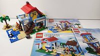 Full view of set showing assembled seaside house, palm tree, minifigure, and three instruction booklets.