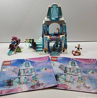 Full set photo showing castle, minifigures, small sled, side build with icicle tree, and two instruction booklets