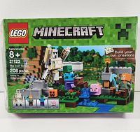 Front view of LEGO Minecraft set 21123 box showing the Iron Golem, Alex and zombie minifigures, baby pig, and build terrain. The box indicates 208 pieces and recommended age 8+.