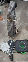 Full view of golf bag on wheels and two Dunlop tennis rackets with a Swingball game base
