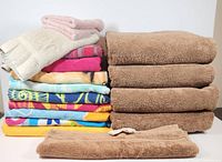 Front view of stacked beach towels with colorful patterns, stacked plush brown bath towels, beige wash cloths and smaller towels on top