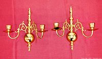 Front view of pair of brass wall candleholders on red fabric background.