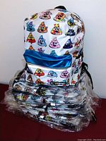 Stack of 12 sealed backpacks with colorful poop emoji prints and blue front pocket.
