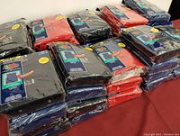 Eighteen unopened packs of Fruit of the Loom boys' sleeveless t-shirts in assorted colors on a table, sealed in original packaging.