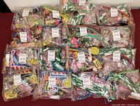 Photo showing 16 sealed party favor bags laid out on a burgundy surface. Each bag contains multiple small toys and novelty items visible through clear plastic.