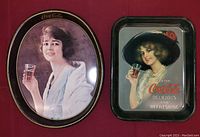 Two vintage Coca-Cola advertisement trays placed on a surface, one oval and one rectangular, showing artwork of women holding Coca-Cola glasses.