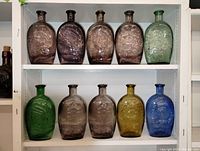 Ten vintage embossed glass bottles arranged on two shelves in varying colors including brown, green, amber, and blue.